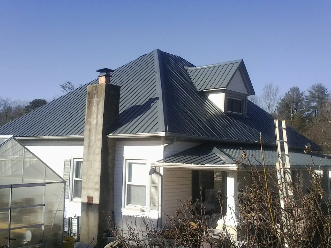 Dark blue standing seam metal roof on a white farmhouse with dormer — Slate & Tile Roof Repair by Roofing Brothers in Lamar