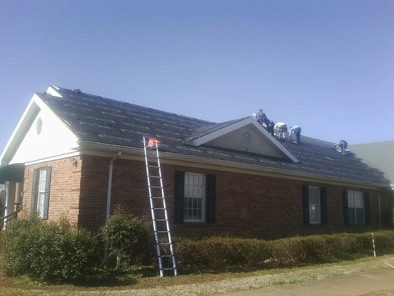 Crew tearing shingles off a brick ranch roof with a ladder set — Emergency Roof Repair work by our crew in Lamar