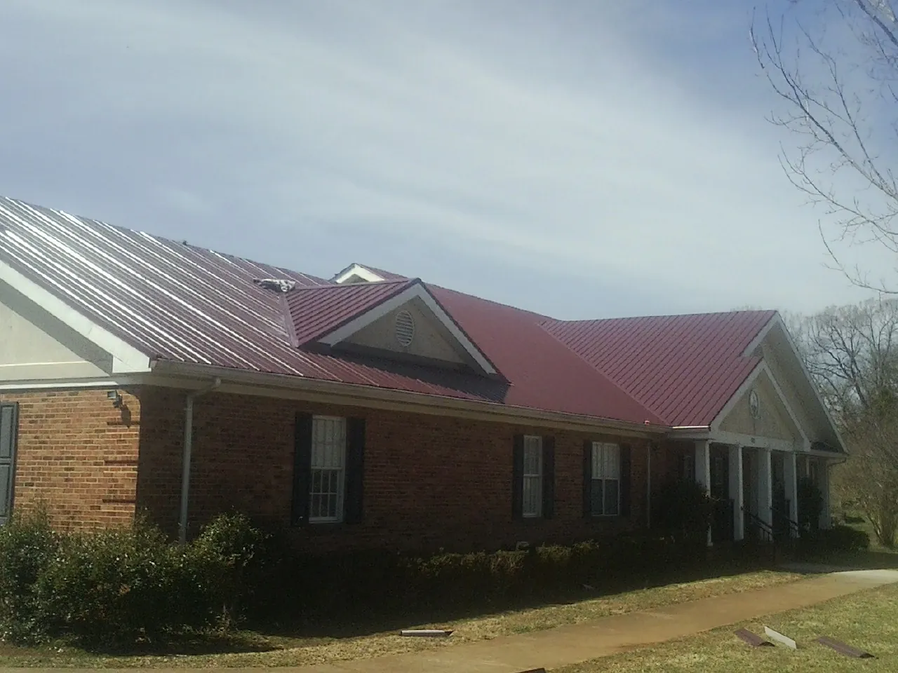 Red metal roof with gabled entries on a long brick building, from a Hail Damage Roof Repair job in Lamar