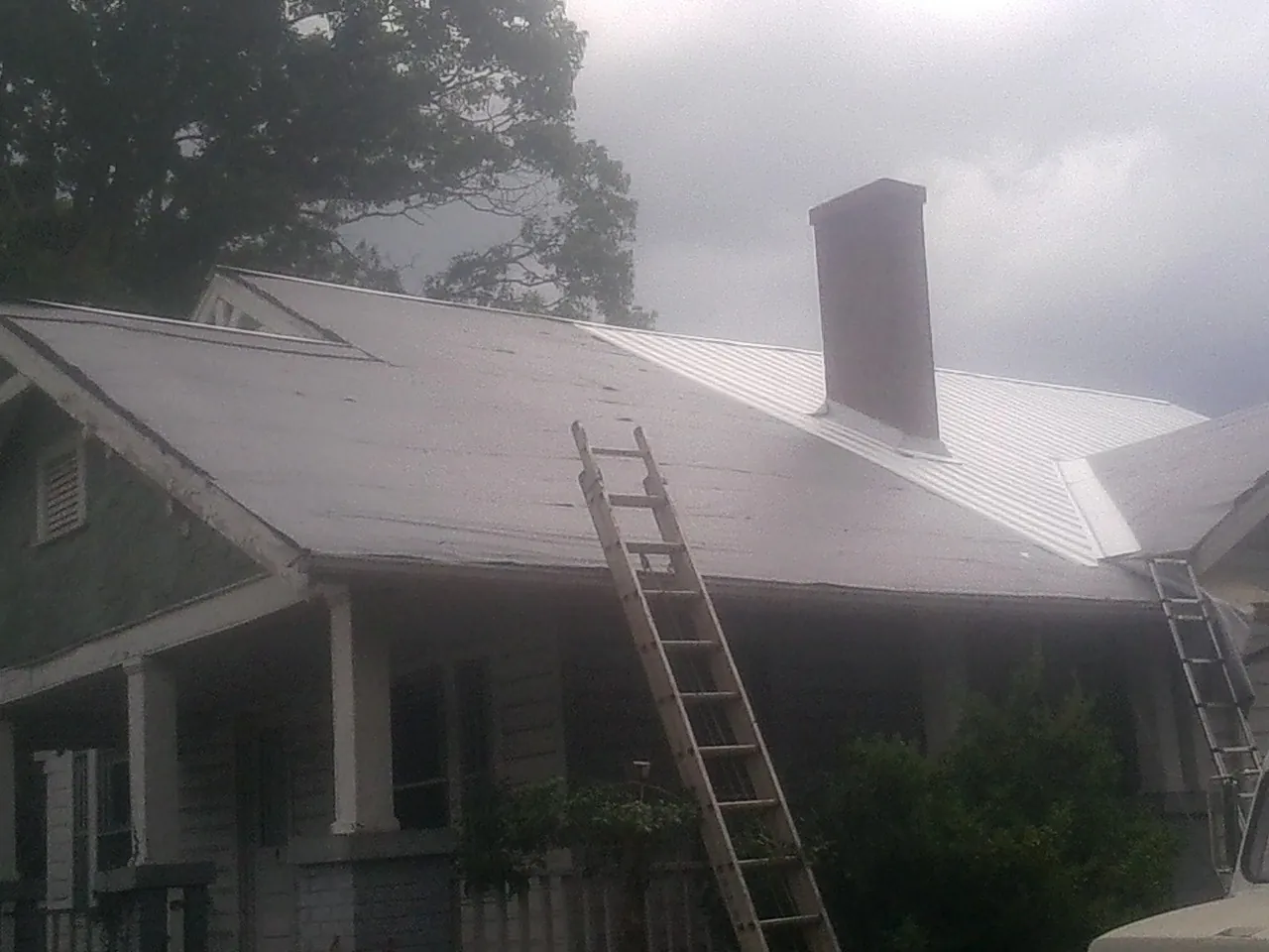 Ladders against a metal roof on an older home with a brick chimney in Lamar